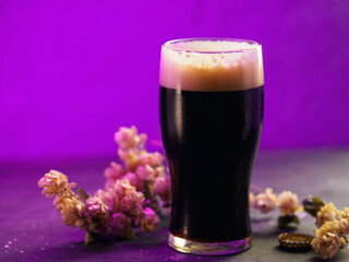 A glass of dark craft beer , porter or stout on a purple neon background