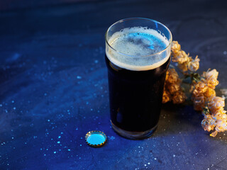 A pint of craft beer stout on a blue background. A glass of dark beer