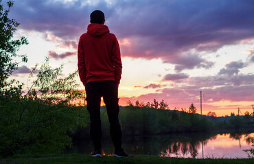 Fototapeta premium A man alone admires a beautiful summer sunset by the river