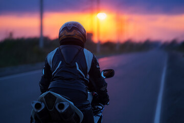 Biker on a fast sports motorcycle on the road. Rear view, colorful sunset. The concept of freedom....