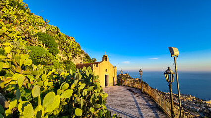Chiesa di San Biagio of Castelmola with panoramic view on coastline of Ionian Mediterranean sea near Taormina, Sicily, Italy, Europe, EU. A field of cactus around the church at sunset golden hour time - obrazy, fototapety, plakaty
