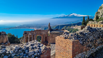 Panoramic view of snow capped Mount Etna volcano on a sunny day seen from the ancient Greek theater of Taormina, island Sicily, Italy, Europe, EU. Travel destination at the Mediterranean sea. Tourism - obrazy, fototapety, plakaty