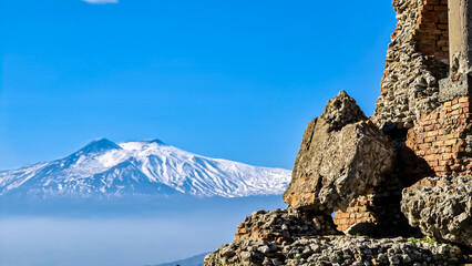 Panoramic view of snow capped Mount Etna volcano on a sunny day seen from the ancient Greek theater of Taormina, island Sicily, Italy, Europe, EU. Travel destination at the Mediterranean sea. Tourism
