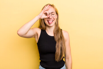 young adult  blonde woman smiling happily with funny face, joking and looking through peephole,...