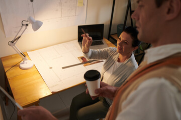 Team of architects drinking coffee and discussing plants and blueprints of new house