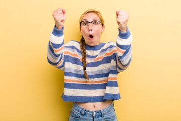 young adult  blonde woman celebrating an unbelievable success like a winner, looking excited and...