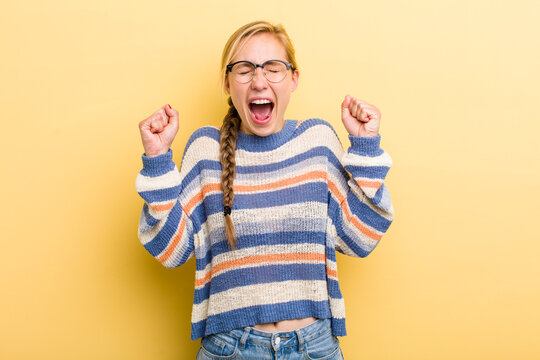 young adult  blonde woman looking extremely happy and surprised, celebrating success, shouting and jumping