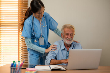 Friendly young woman nurse helping senior man in wheelchair using laptop, Elderly male patient surfing on Internet at nursing home.