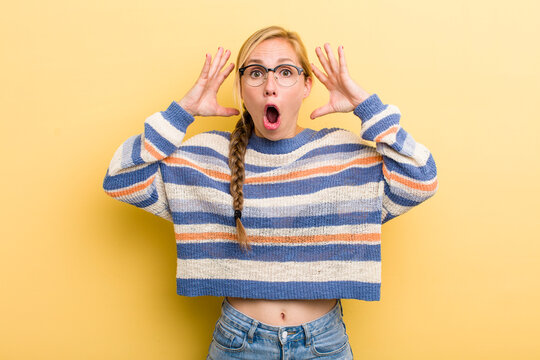 young adult  blonde woman screaming with hands up in the air, feeling furious, frustrated, stressed and upset