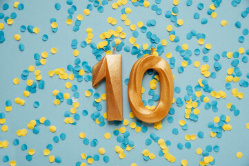 Number 10 ten golden celebration birthday candle on yellow and blue confetti Background. Ten years...