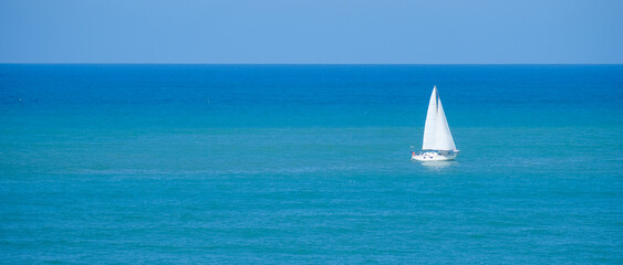 Single sailboat on the calm blue waters of the Mediterranean Sea of the coast of Italy.