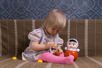 A small child in clothes from the era of the USSR and with Soviet toys sits on the sofa,...