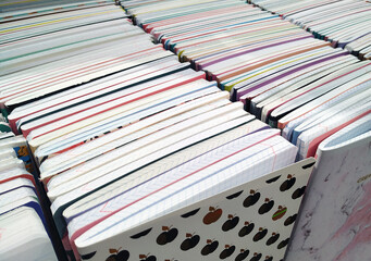 School notebooks for writing are stacked in rows, edges up, on a stand in a stationery store. School supplies. - obrazy, fototapety, plakaty
