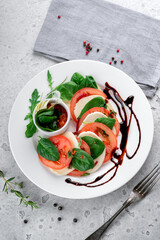 Caprese salad with tomatoes, mozzarella cheese, basil and balsamic sauce on a white plate on the kitchen table.