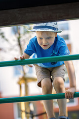 Obraz premium Happy little boy having fun in an urban playground, he climb on the green tube ladders.