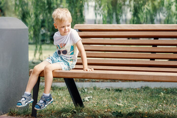 Small child plays in park. Kid is sitting on a park bench. - Powered by Adobe