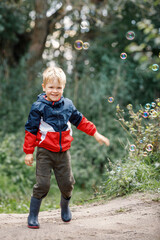 Cute happy little boy playing with soap bubbles in park.