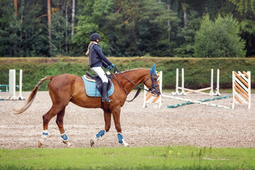 Training process. Young teenage girl riding bay trotting horse on sandy arena practicing at...