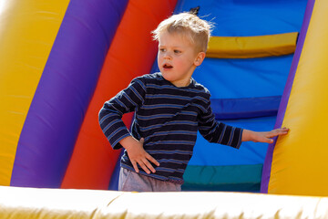 Child on colorful playground trampoline. Kid jump in an inflatable bounce castle at a kindergarten...