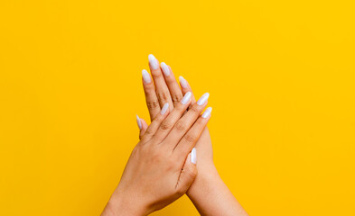 Two clean white hands and beautiful nails intertwined on a yellow background.