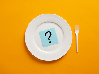 Notepaper with question mark symbol on a white plate with yellow background. Nutrition and diet