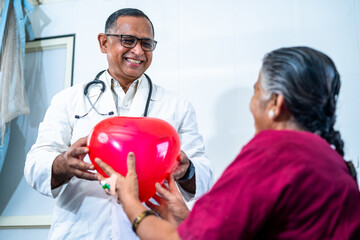 Happy smiling doctor giving balloon heart to recovered senior patient at hospital - concept of...