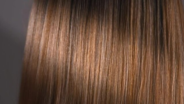 Hair. Beautiful healthy long smooth flowing brown hair close-up texture. Dyed straight shiny hair background, coloring, extensions, cure, treatment concept. Haircare. Slow motion 4K UHD video