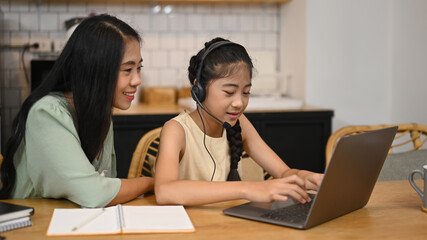 Asian mom helping her daughter doing homework, learning online at kitchen table