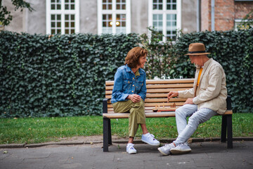 Happy senior couple sitting on bench and playing chess outdoors in park.