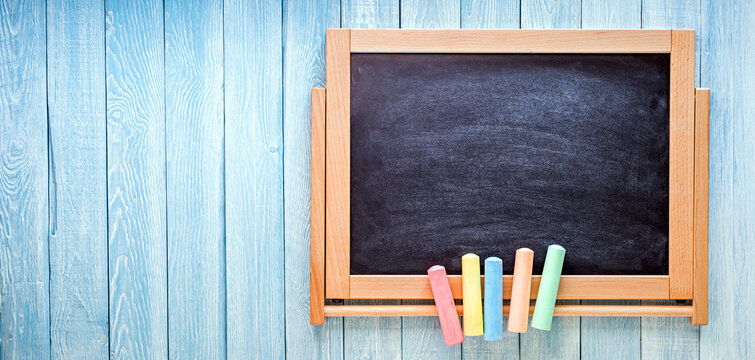 Small black board with colored chalks on blue wooden planks. Back to school concept