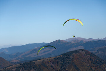 Paragliders flying in the blue sky with mountain in background.