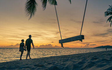 Silhouettes of a couple walking on a sandy tropical beach at sunset. 