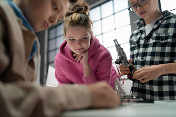 Group of kids working together on project with electric toys and robots at robotics classroom, close up for girl
