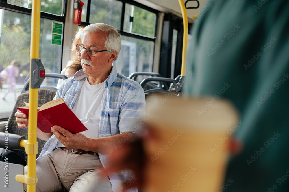 Poster Senior man reading book while riding bus