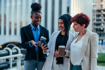 Three beautiful multiracial businesswomen looking at a phone