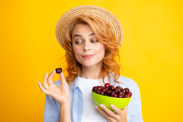 Young woman eats sweet cherries. Portrait of a beautiful girl with cherry on yellow background....