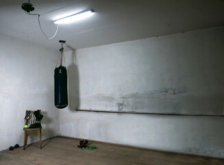 a punching bag in an empty boxing gym with a bare orange wall in the background. An old black...