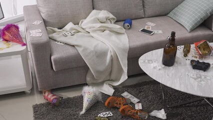 view of messy living room after a riotous drinking party. disorder, chaotic interior with beer bottles, shoes, cards scattered all over the room. decadent lifestyle concept