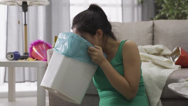 asian female with rubbish bin drinking an excess of alcohol feels terribly sick in the morning. taiwanese girl wiping her mouth feeling miserable after throwing up violently