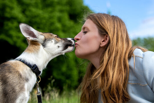 portrait of blond woman kissing her puppy dog outdoors
