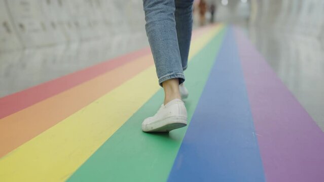 Young gen z teen queer transgender people playful steps walk dance relax move fun enjoy music on colorful stripes flag street. Proud of LGBTQ LGBT gay culture sign bisexual festival march parade.
