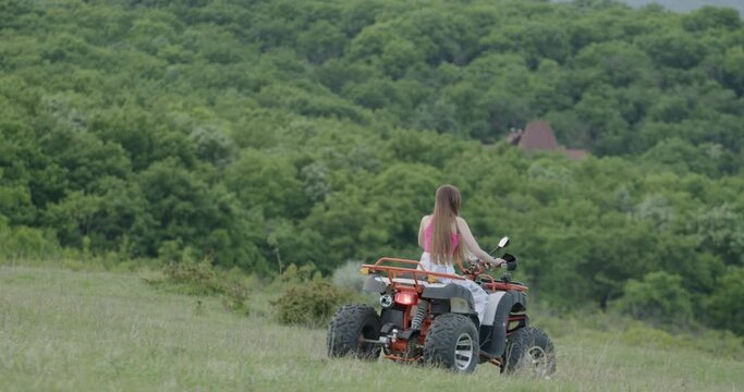 Free woman rides a quad near the forest on a plain of green grass. ATV off-road adventure. The girl drives a Quad Cycle, adventure, travel, tourism. Outdoor activities in summer, outdoor travel