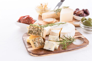 Cheese board with selection of cheeses served with olives, sun-dried tomatoes and herbs on white...
