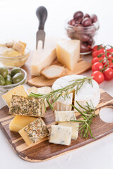 Cheese board with selection of cheeses served with olives, tomatoes and herbs on white table background. Cheese plate for aperitif - brie, dorblu, gorgonzola, camembert and parmesan