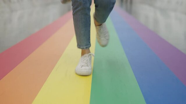 Young gen z teen queer transgender people playful steps walk dance relax move fun enjoy music on colorful stripes flag street. Proud of LGBTQ LGBT gay culture sign bisexual festival march parade.