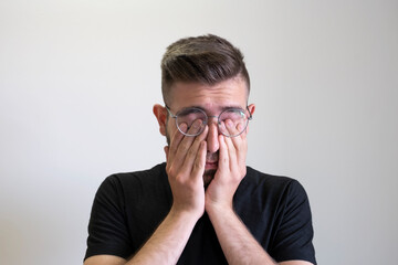 Young man rubbing his eyes, portrait of tired young man rubbing his eyes isolated on grey background. Caucasian, brown haired teenage boy wearing glasses. - Powered by Adobe