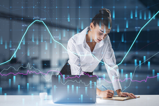  businesswoman standing at desktop using laptop with abstract glowing forex graph on blurry office interior background with candlestick. Invest, trade and broker concept. Double exposure.