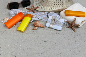 Komposition Sonnenschutz: Flaschen mit Sonnencreme, Sonnenbrille und Hut im Sand .