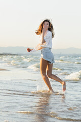 Fototapeta na wymiar Young woman blowing air kiss while running on sea coast.
