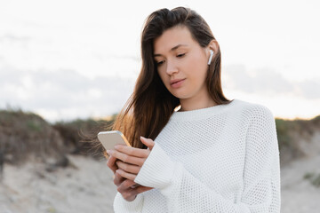 Young woman in earphone using cellphone on beach in evening.